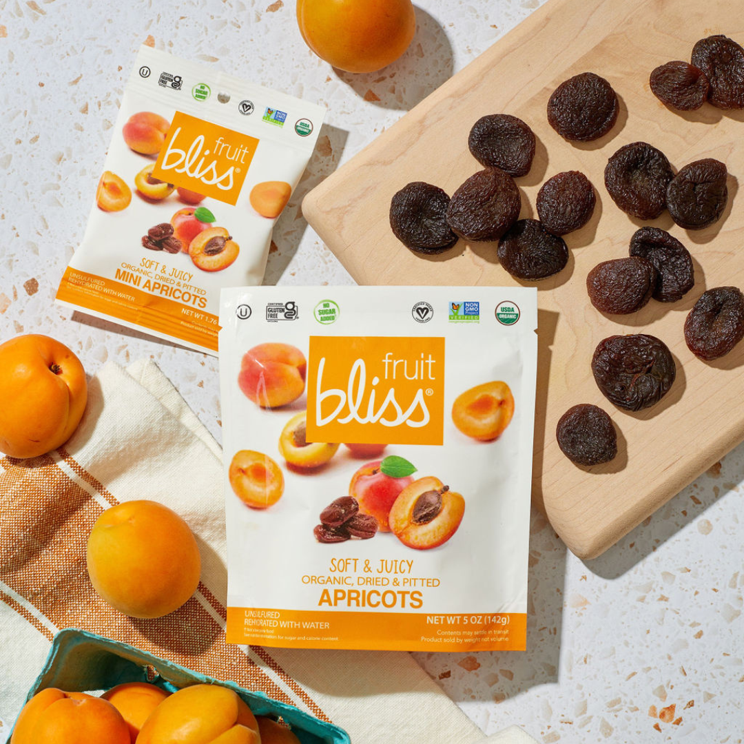 Two packages of Fruit Bliss Mini Apricots with dried apricots on a wooden board.